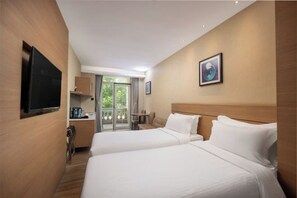 Habitación de hotel con dos camas, televisión, kitchenette pequeña y balcón con vistas a zonas verdes.