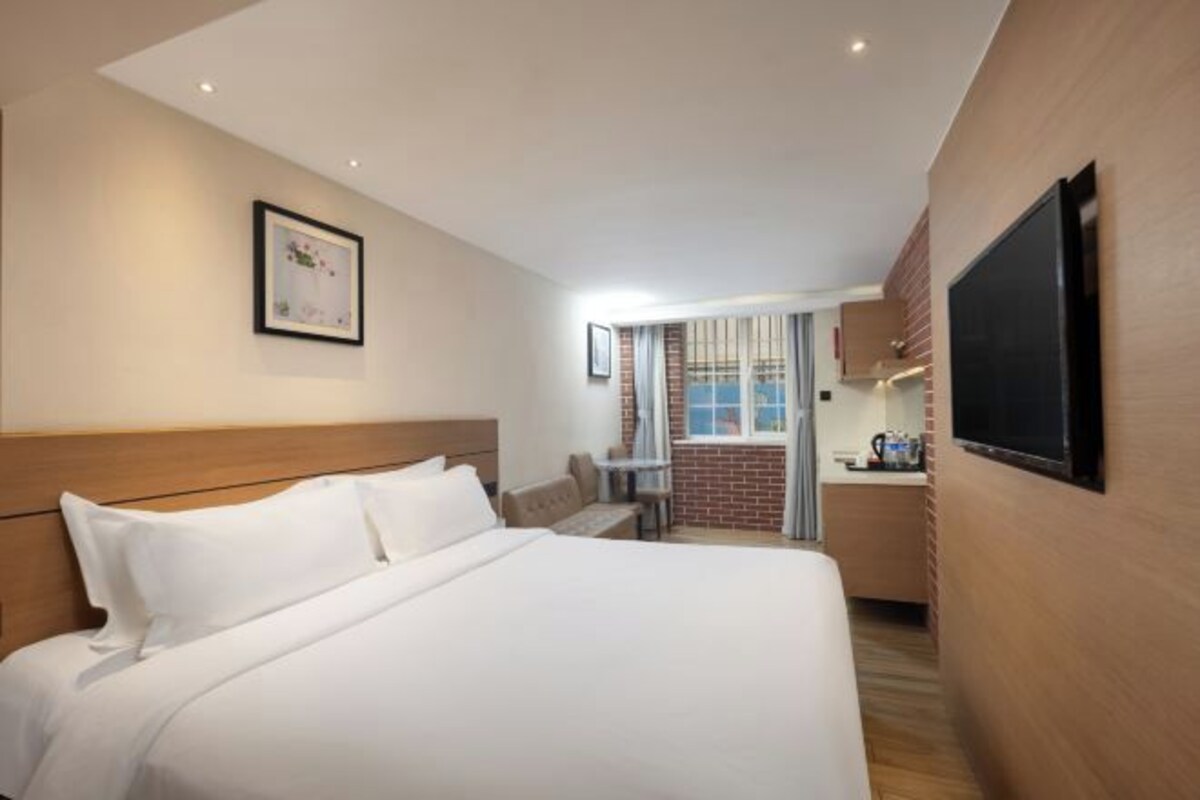 Una habitación de hotel con una cama, televisor, una mesita y una kitchenette.