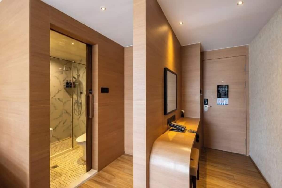 A modern hotel room with a wooden floor, a glass shower enclosure, a wooden bench, and a wall-mounted TV.