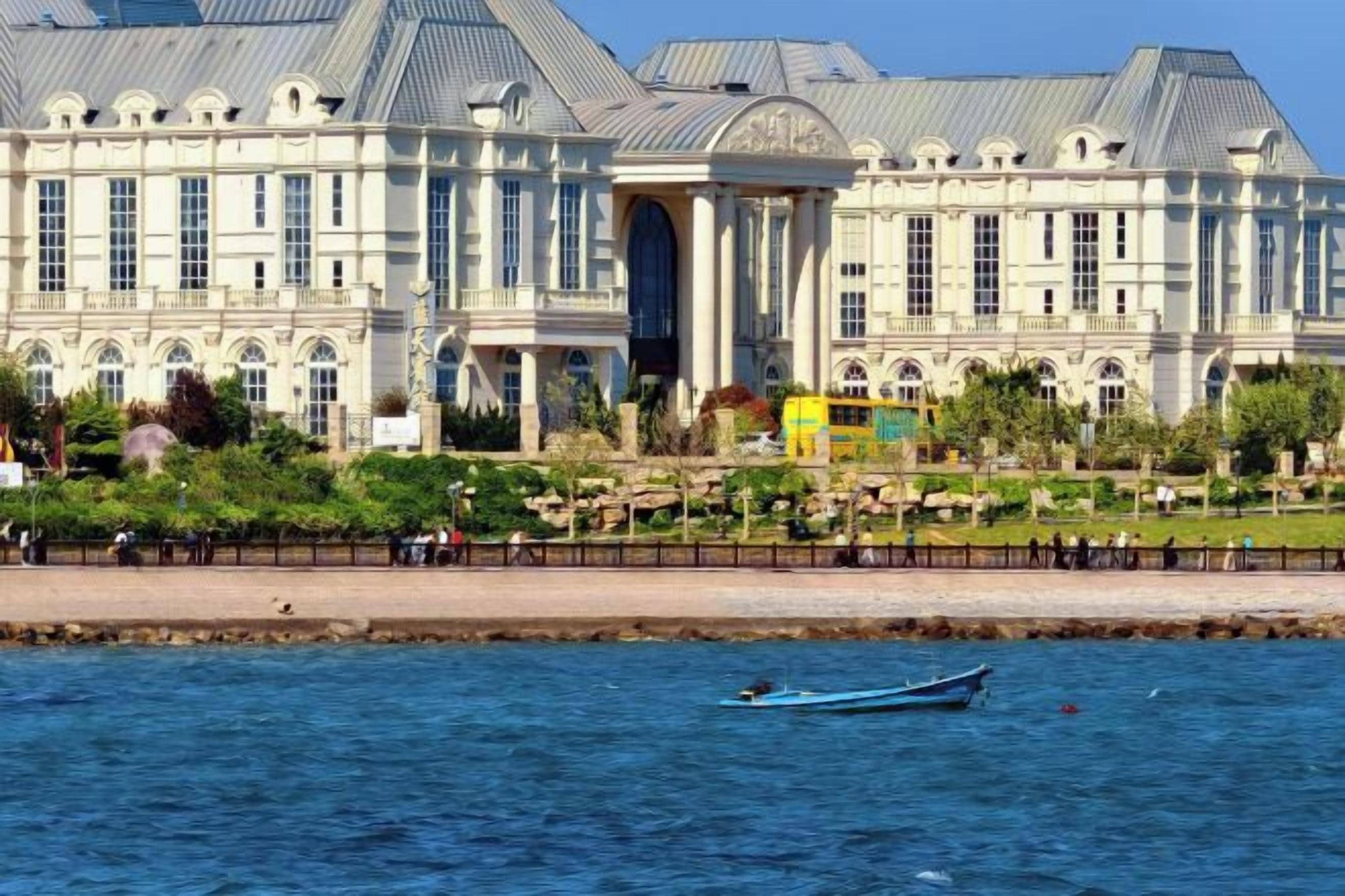 A large building with a classical architectural style, a waterfront, and a small boat on the water.