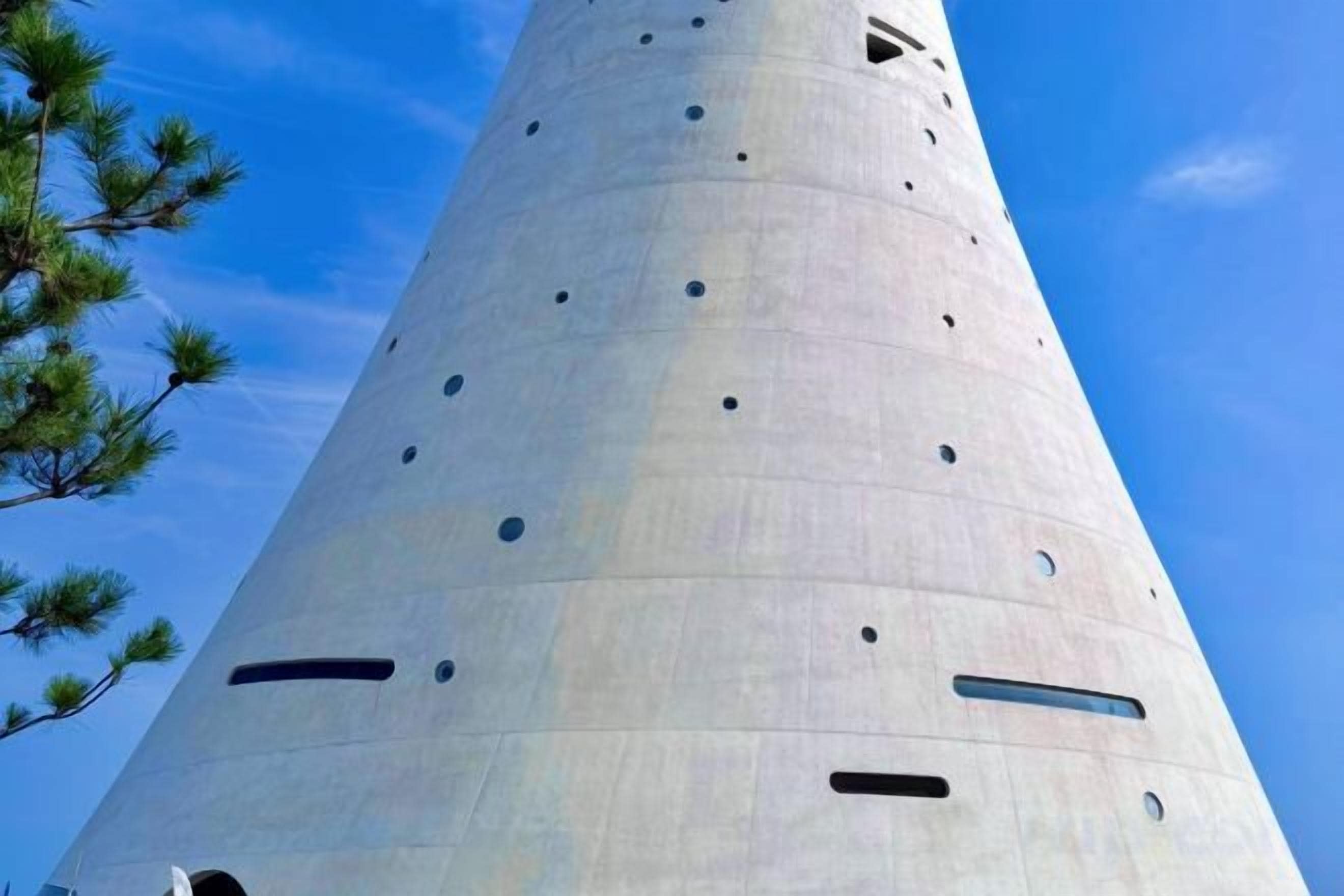 A tall, cylindrical structure with multiple circular openings and a few rectangular cutouts.