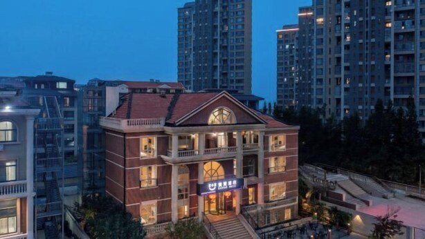 A multi-story building with a prominent entrance and a balcony, surrounded by high-rise residential buildings. - Zanzan Hotel (Yantai)