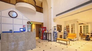 A hotel lobby with a reception desk, a clock, a large vase, and seating area. - Zanzan Hotel (Yantai)