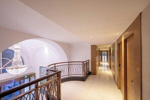A hotel corridor with a curved railing, a chandelier, and a view of the hallway. - Zanzan Hotel (Yantai)