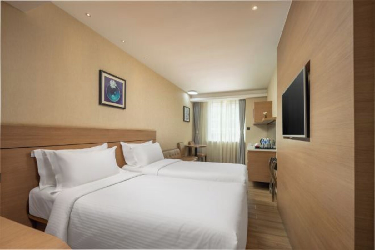 Habitación de hotel con cama doble, escritorio, silla, televisor y ventana con cortinas.