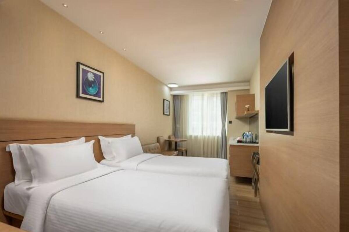 A hotel room with a double bed, a desk, a chair, a TV, and a window with curtains.