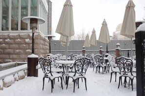 Outdoor seating with snow-covered chairs and tables, a brick wall, and umbrellas. - Zanzan Hotel (Yantai)