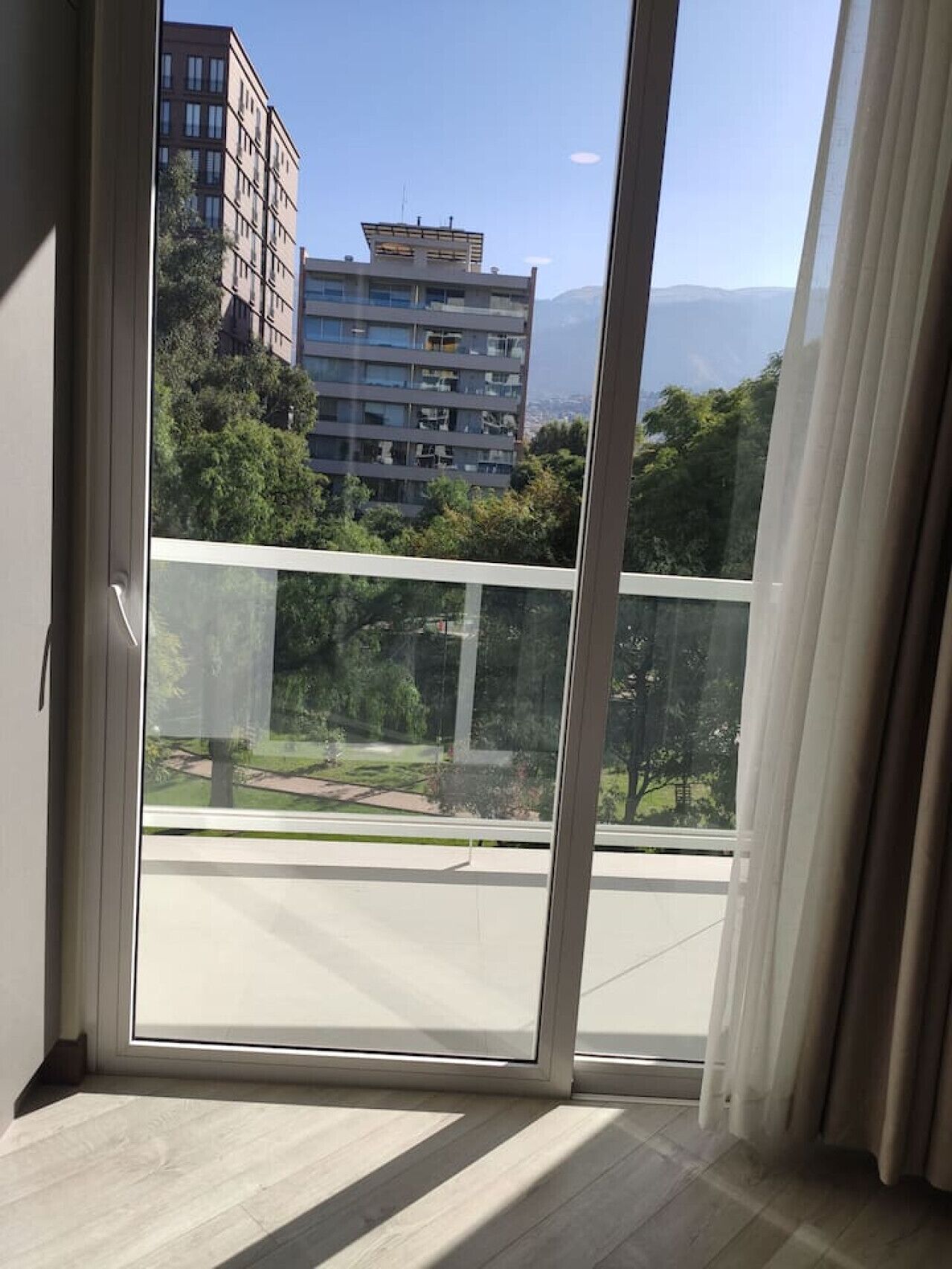 A view from a balcony with a glass door, overlooking a cityscape with buildings and greenery.
