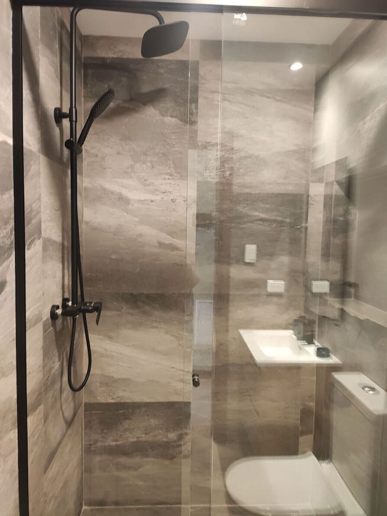 A glass-enclosed shower stall with a handheld showerhead and a wall-mounted faucet.