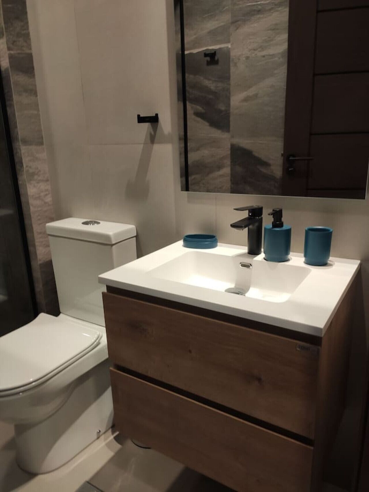 Un baño moderno con inodoro blanco, un lavabo de mármol y muebles de madera.