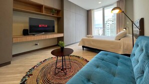 A modern hotel room with a bed, a TV on a wooden shelf, a round table with a plant, and a blue sofa. - Exclusive modern apartment with unbeatable location (Cochabamba)
