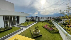 A rooftop garden with a modern building, a large planter with a tree, and a view of the city skyline. - Exclusive modern apartment with unbeatable location (Cochabamba)