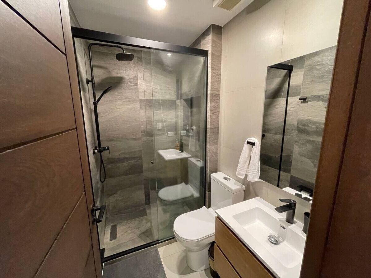 A modern bathroom with a glass-enclosed shower, a toilet, and a sink with a mirror.