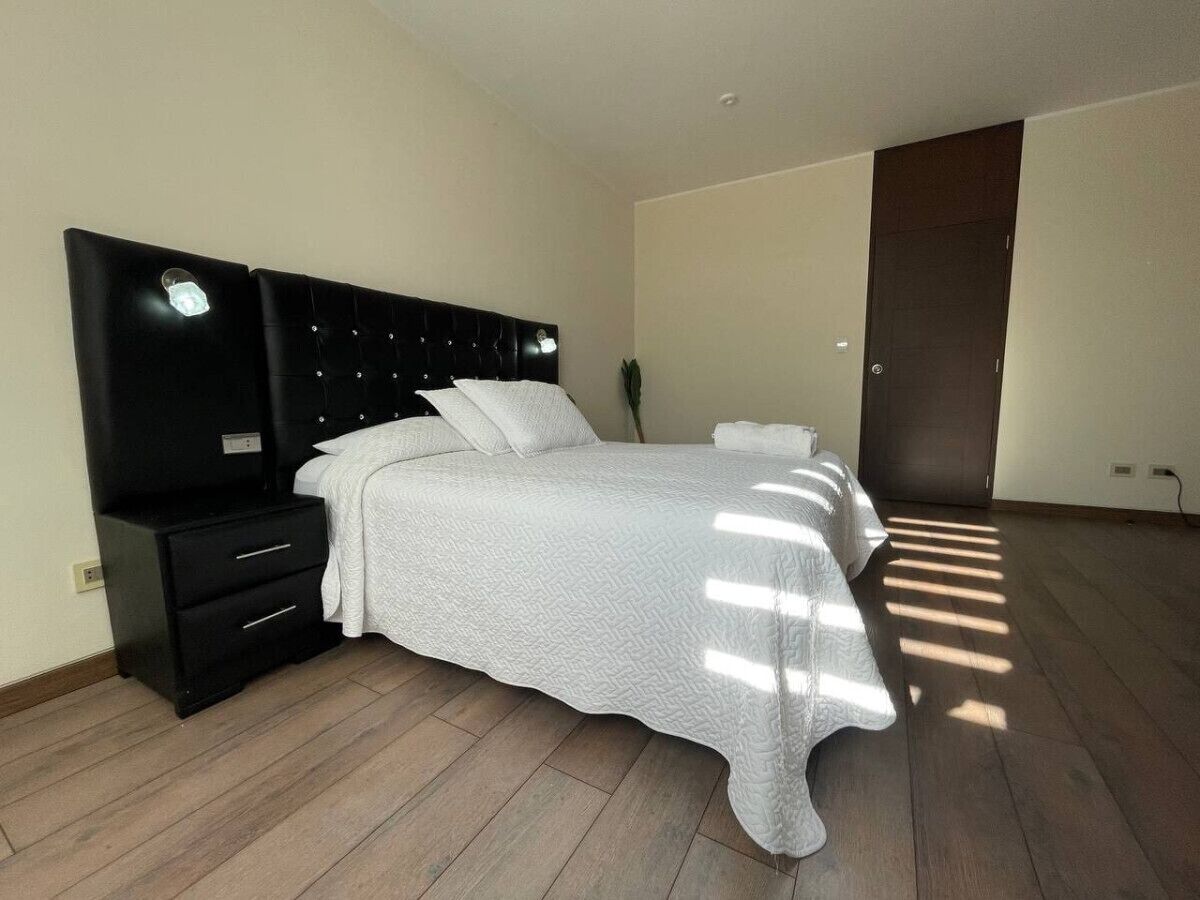 Un dormitorio con una cama, una mesita de noche, un aparador y una puerta oscura.