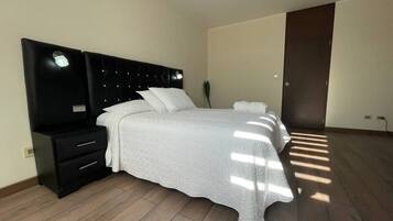 Un dormitorio con una cama, una mesita de noche, un aparador y una puerta oscura.