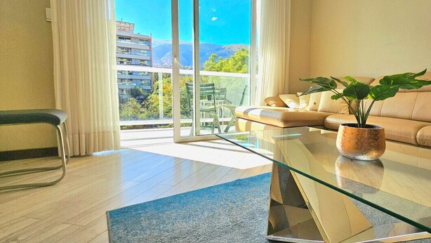 Een moderne woonkamer met een glazen salontafel, een beige bank en een potplant.