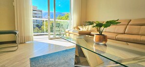Una sala de estar moderna con una mesa de centro de vidrio, un sofá color beige y una planta en maceta.