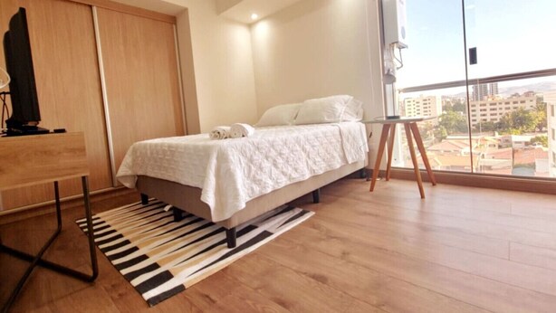 Um quarto com uma cama, uma televisão, uma janela grande e vista para a cidade.