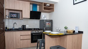 Uma cozinha compacta com armários de madeira, fogão preto, geladeira, micro-ondas e um pequeno balcão com banquetas.
