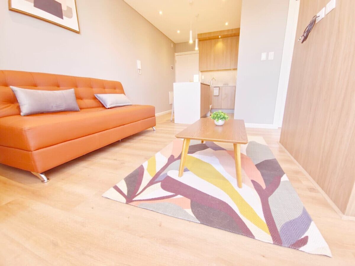 A modern living room with an orange sofa, a wooden coffee table, and a colorful rug.