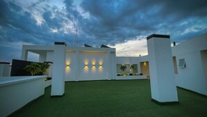 Terraço no telhado com grama sintética, paredes brancas e luminárias modernas.
