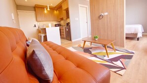 Uma sala de estar moderna com um sofá, uma mesinha e uma cozinha ao fundo.