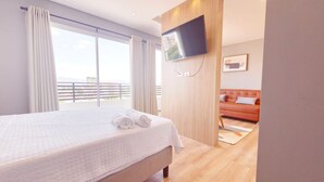 Quarto de hotel com uma cama grande, televisão na parede e vista da cidade pela janela.
