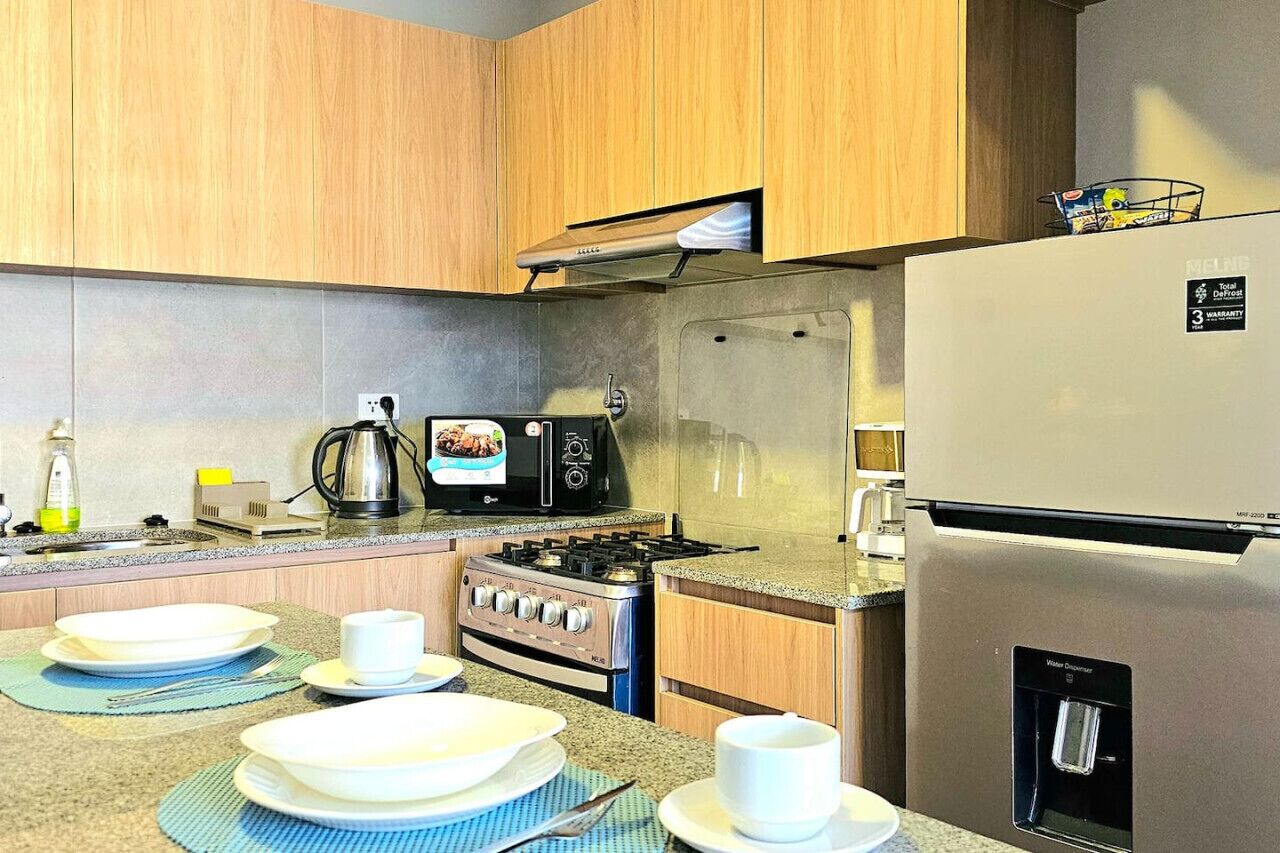Une cuisine moderne dotée de meubles en bois, d’un réfrigérateur en acier inoxydable, d’une cuisinière à gaz, d’un four à micro-ondes et d’un distributeur d’eau.