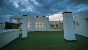 Une terrasse sur le toit avec un revêtement de gazon synthétique, des murs blancs et des appliques murales illuminées.