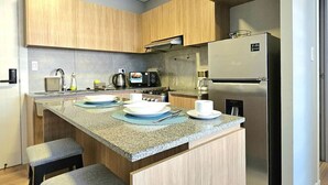 Une cuisine moderne avec des meubles en bois, un plan de travail en granit, un four encastré, un réfrigérateur et une machine à café.