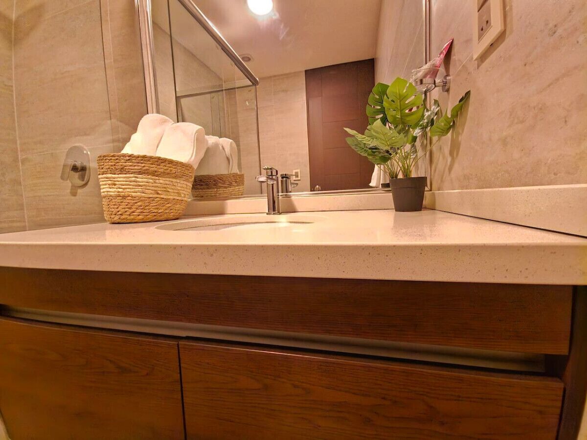A bathroom with a wooden vanity, a sink, a mirror, a basket with towels, and a potted plant.