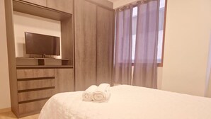 Ein Schlafzimmer mit Bett, Fernseher auf einem Schrank, Kleiderschrank und einem Fenster mit Vorhängen.