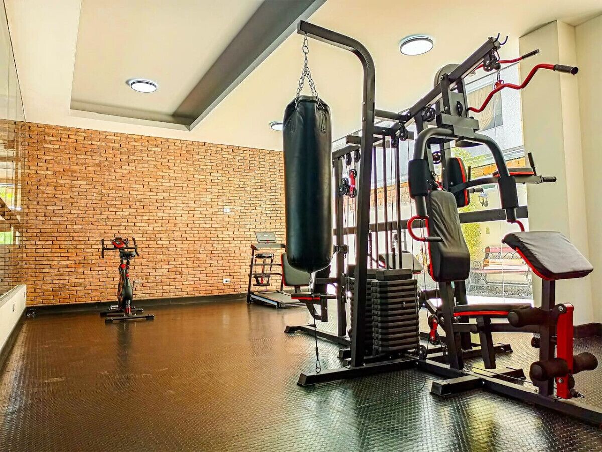 Een sportschool met een bakstenen muur, diverse fitnessapparaten en een bokszak.
