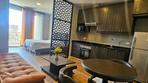 A compact hotel room with a bed, a seating area with a table and chairs, a kitchenette, and a view of the outside.