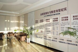 A lobby with a reception desk, seating area, and informational posters on the wall. - Huayi jingxuan Hotel (Guyuan County)