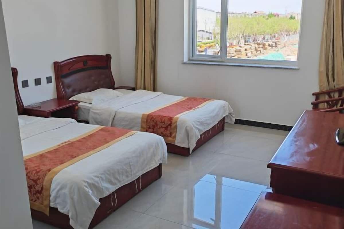A hotel room with two beds, a desk, and a window with a view of a construction site.