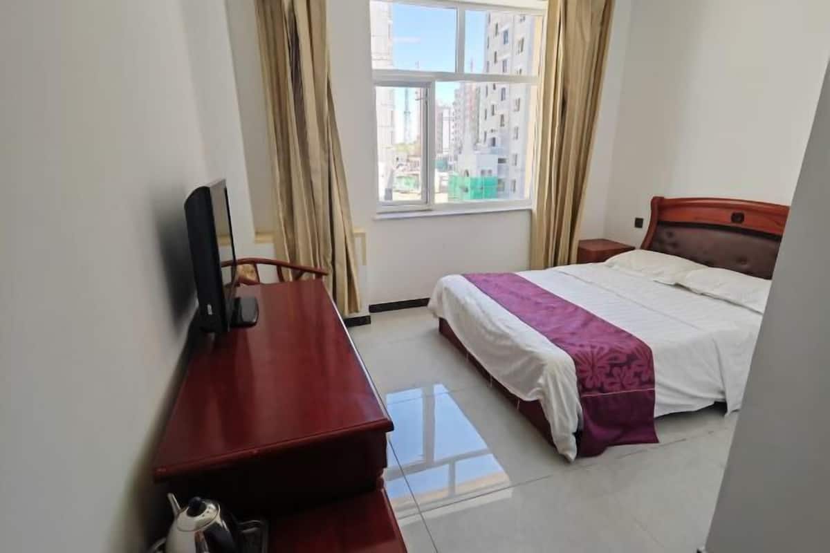 A hotel room with a bed, a desk, a TV, and a window with curtains.