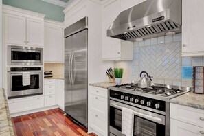 Uma cozinha moderna com eletrodomésticos de aço inoxidável, armários brancos e backsplash de azulejos em padrão herringbone.