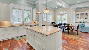 A spacious kitchen with white cabinets, a large island, and a dining area with a blue couch. - POOL, ROOF DECK, ELEVATOR, 5 MIN TO THE SURF! (Isle of Palms)