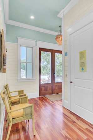 A room with a wooden floor, a wicker chair, a door with a window, and a hanging light fixture.
