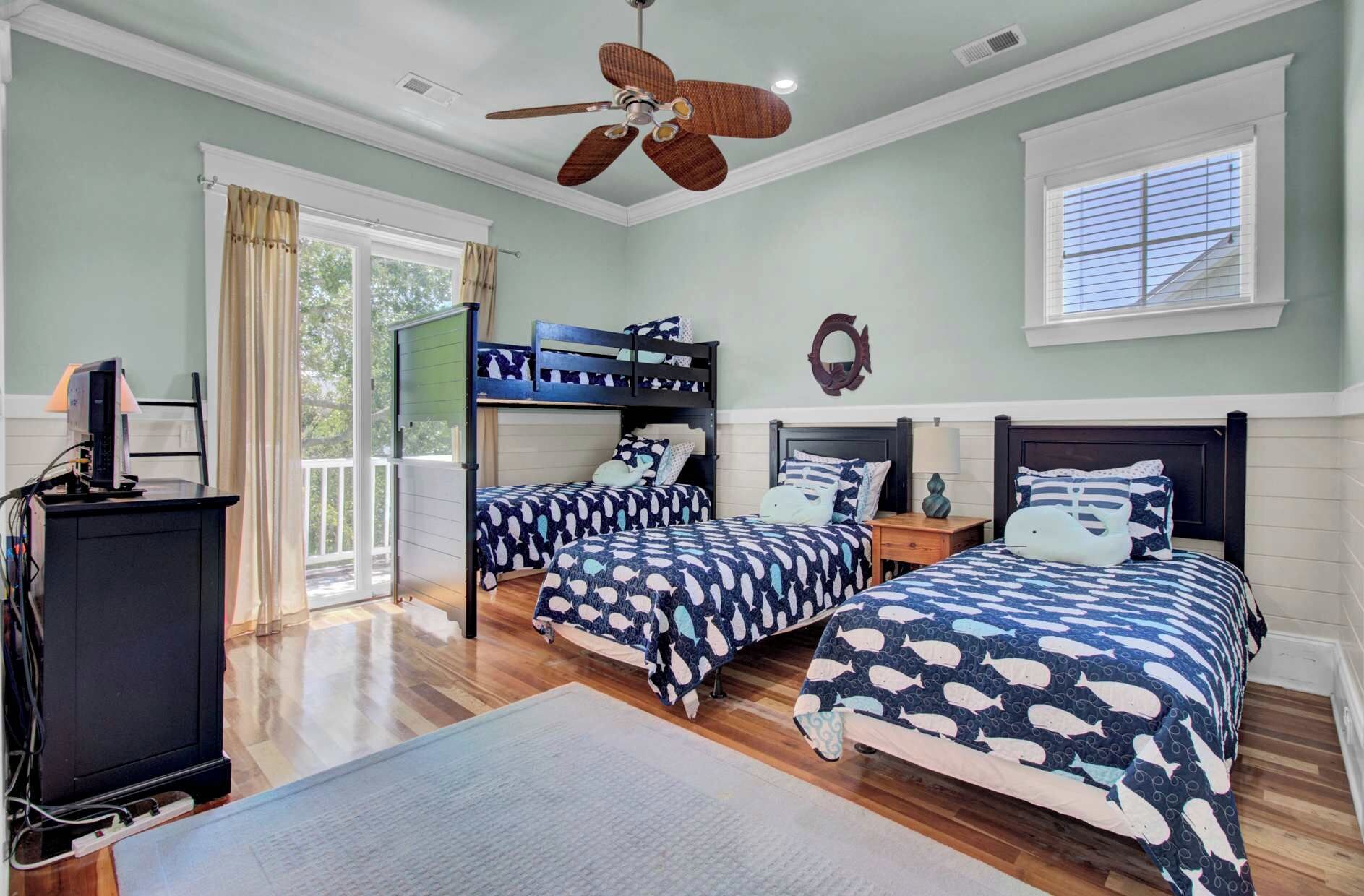 Une chambre avec deux lits superposés, un ventilateur de plafond, un bureau avec un ordinateur et une fenêtre avec des stores.