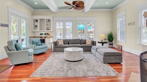A spacious living room with a large grey sectional sofa, a round coffee table, and a ceiling fan. - POOL, ROOF DECK, ELEVATOR, 5 MIN TO THE SURF! (Isle of Palms)