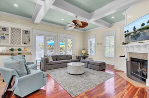 A spacious living room with a fireplace, a ceiling fan, and a large window overlooking a balcony.