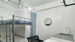 Una camera del dormitorio con letti a castello, una scrivania, una sedia, uno specchio rotondo e un lavandino.