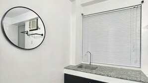 Un bagno con uno specchio rotondo, un lavandino e una finestra con persiane.
