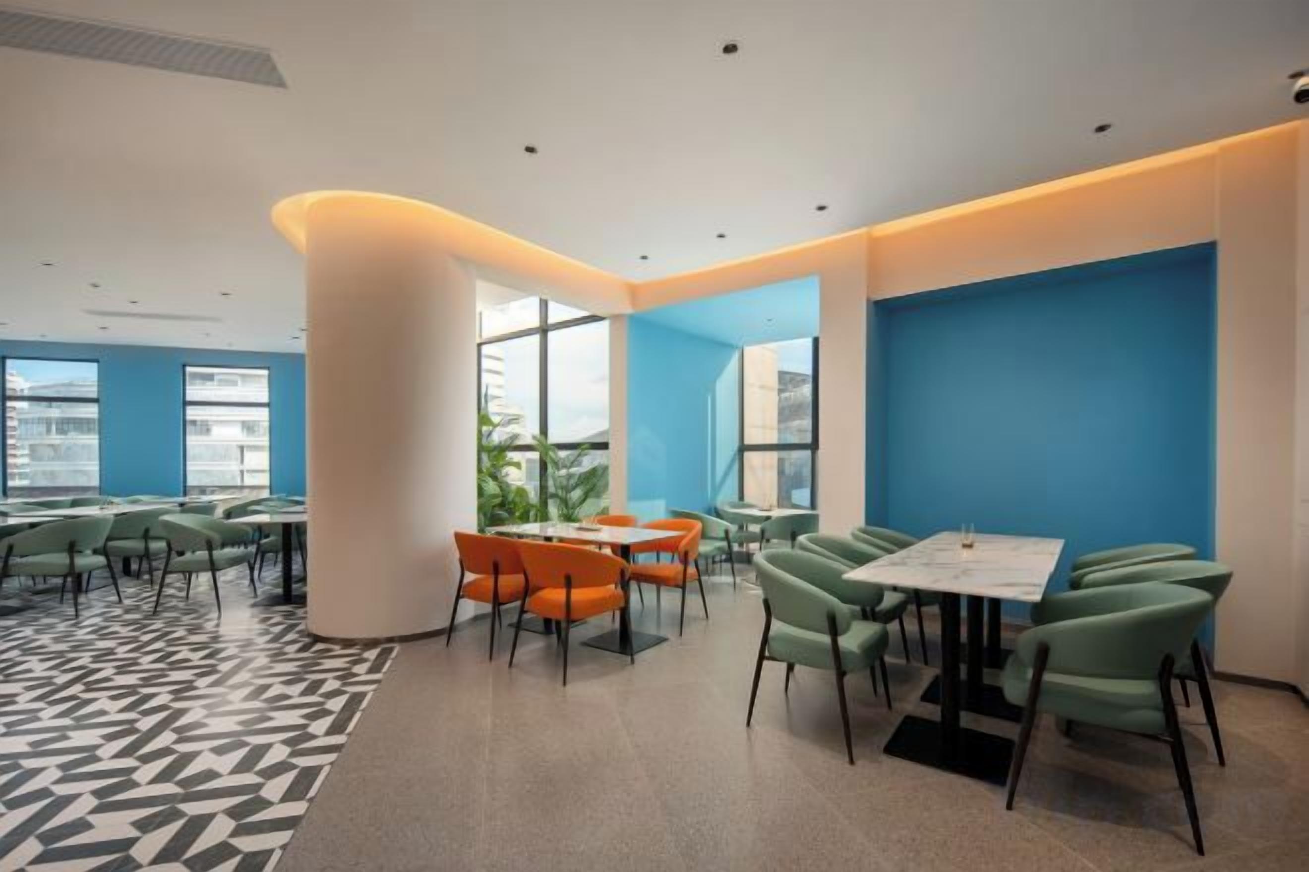 A modern dining area with tables and chairs, large windows, and a blue accent wall.
