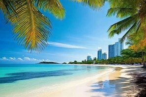 A beach with clear water, palm trees, and buildings in the background. - Tianyi East Ring Hotel (East High-speed Railway Station) (Haikou)