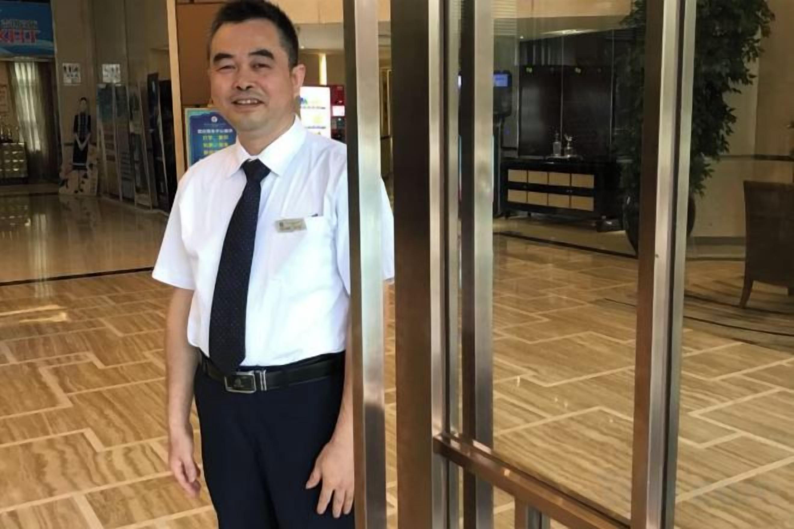 A man standing in a lobby with a glass door and a wooden floor.