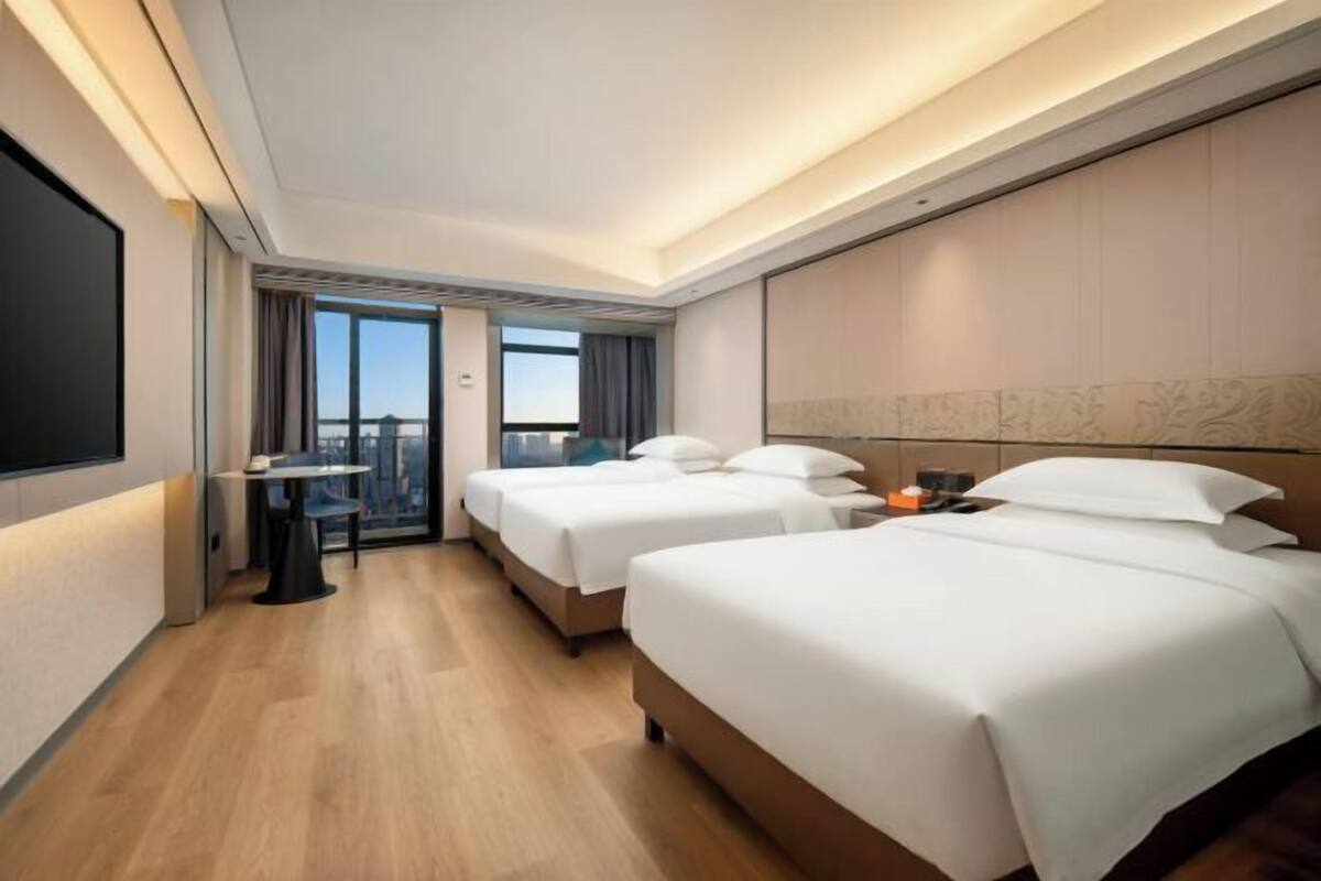 Ein Hotelzimmer mit zwei Betten, einem Schreibtisch, einem Stuhl und einem großen Fenster.