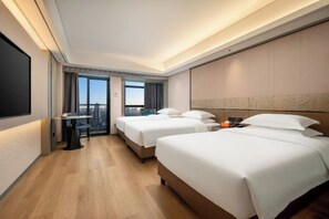 Una habitación de hotel con dos camas, un escritorio, una silla y un ventanal grande.